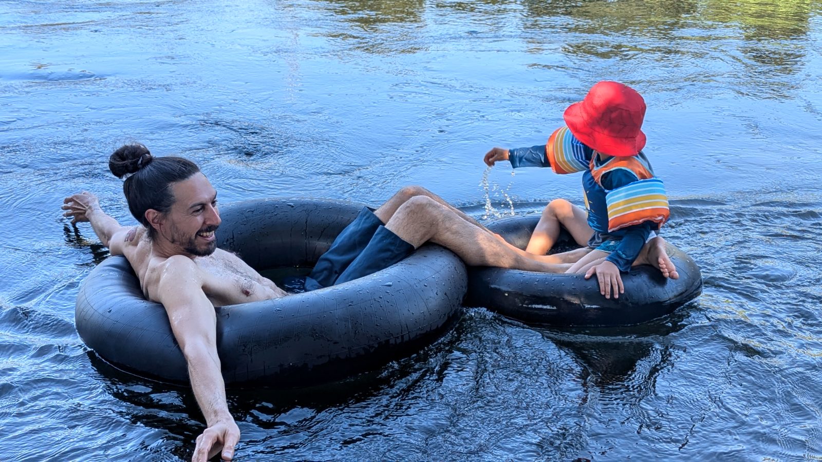 A dad and his toddler drift side by side in black tubes