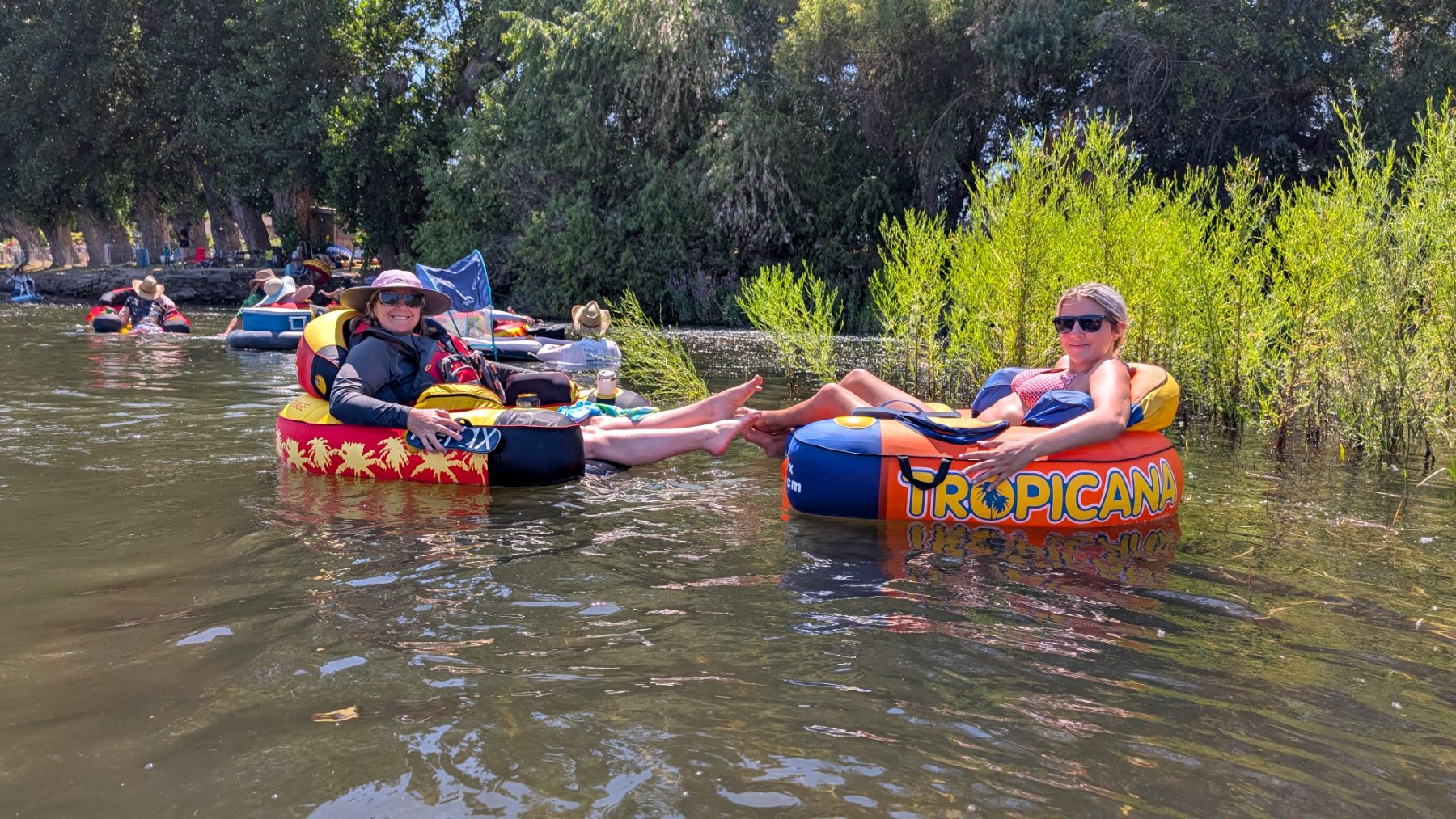 Two floaters relax with their feet up along a leafy bank
