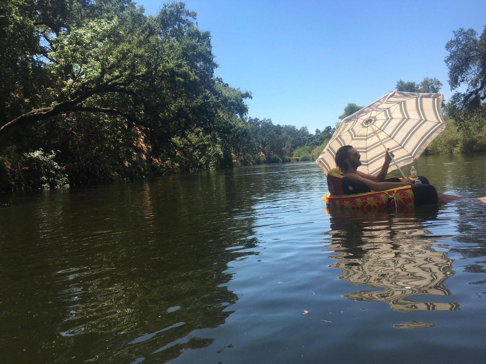A tuber drifts under a sun umbrella on a glassy bend of the Kings River