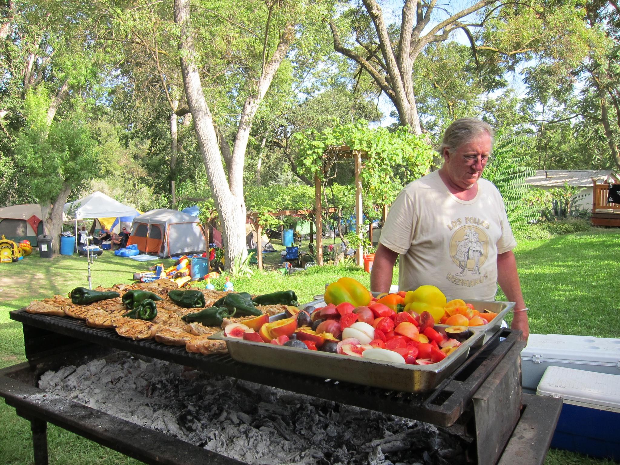 The grill master tending tri-tip and peppers over a bed of coals